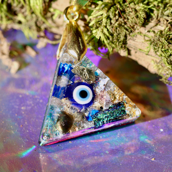 Triangular pendant with evil eye design on a reflective surface