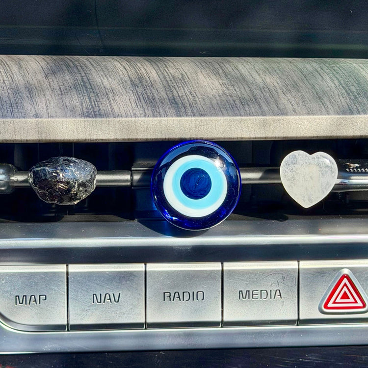 Car dashboard with control buttons and a clear quartz crystal heart, apache tear crystal and blue evil eye glass car accessory 