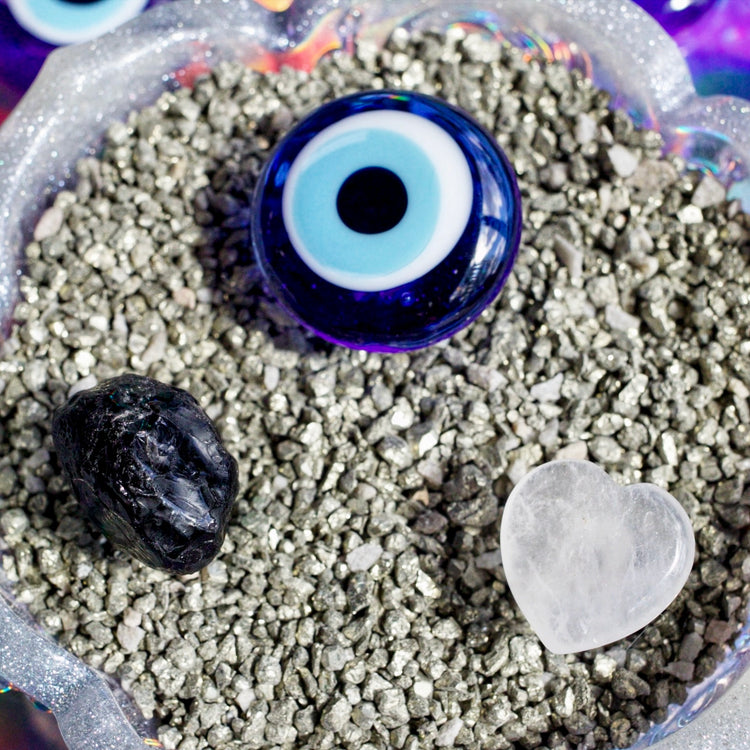 Blue evil eye bead with black stone and crystal on a bed of small stones