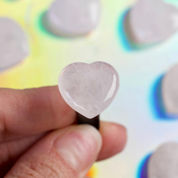 Heart-shaped pink stone held between fingers against a colorful background