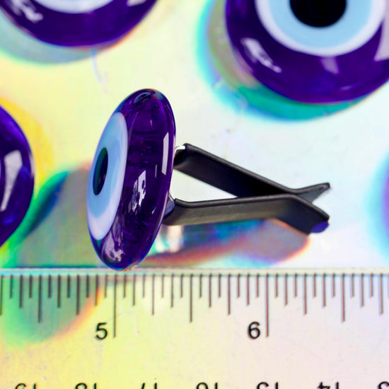 Blue eye-shaped object with a black clip on a colorful background with a ruler for scale.