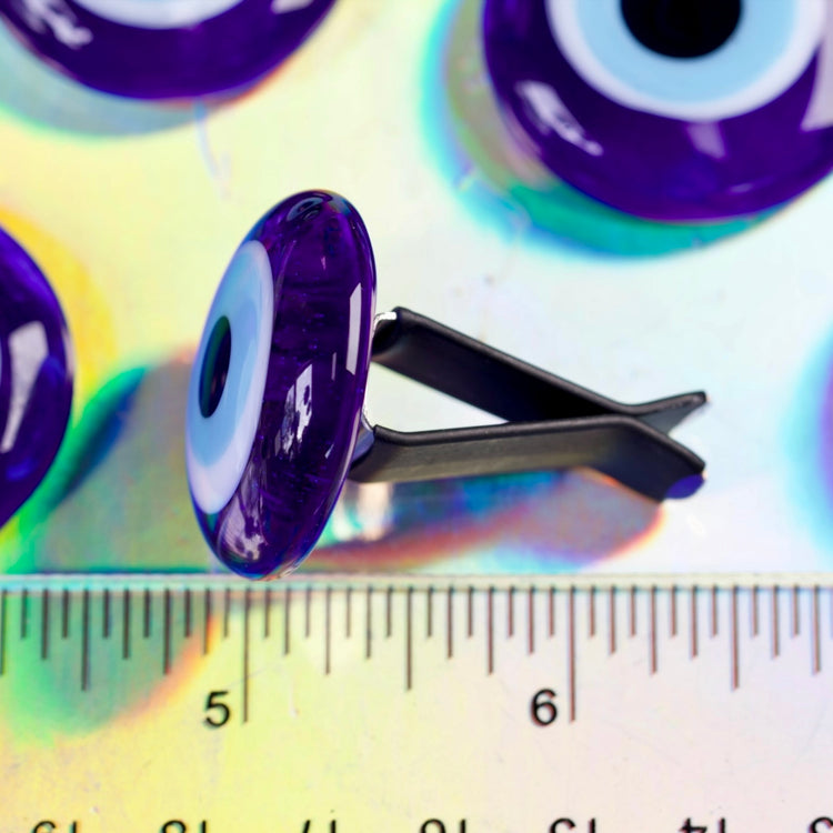 Blue eye-shaped object with a black clip on a colorful background with a ruler for scale.