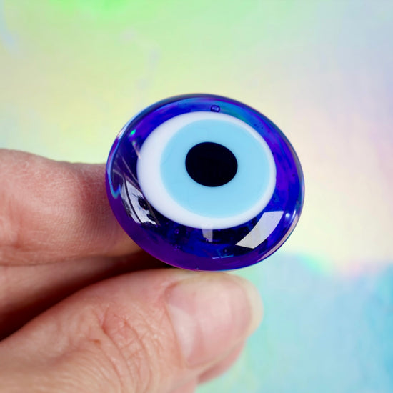 Hand holding a blue glass eye with a white and black center against a colorful blurred background