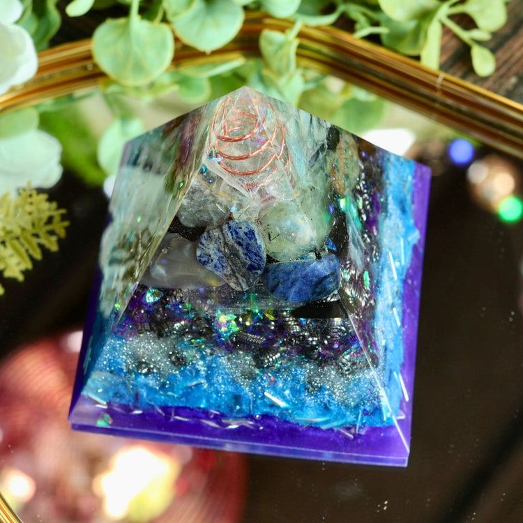 Crystal pyramid with a small figurine on a reflective surface with flowers in the background